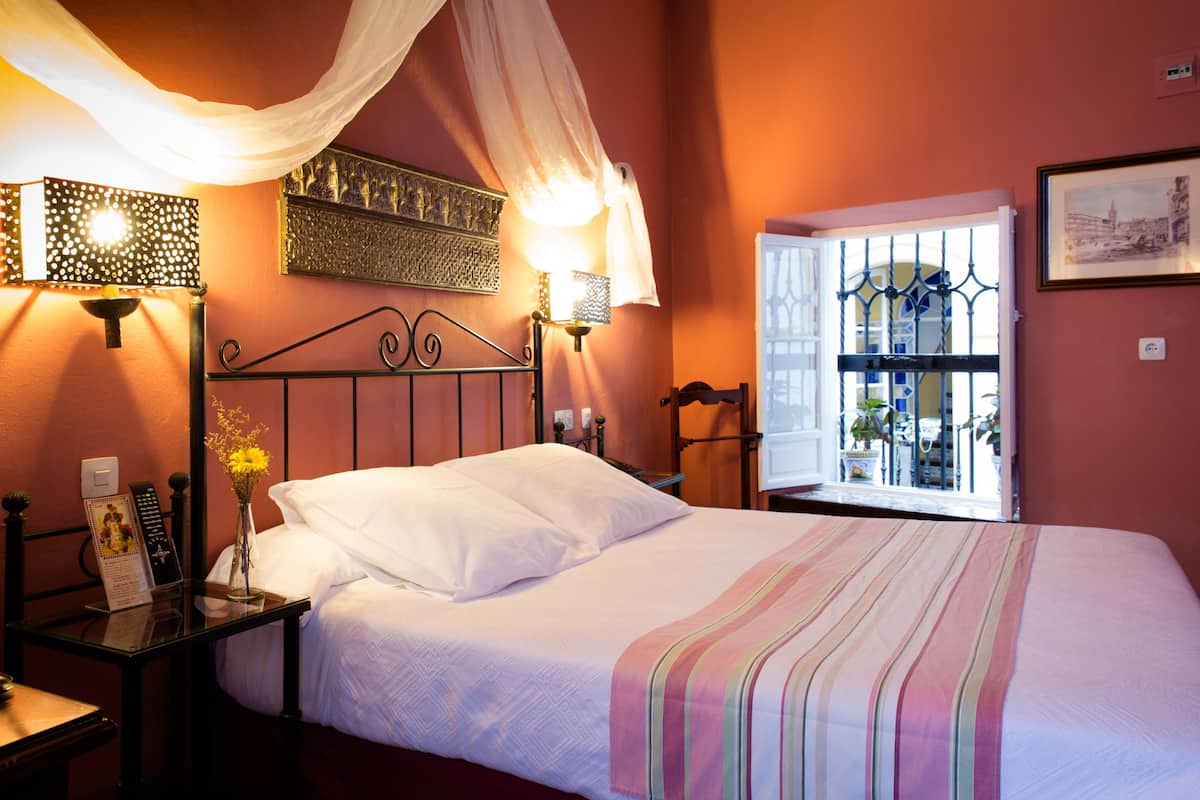 Una cama bien hecha con un edredón a rayas, una mesita de noche con una lámpara y una ventana con vistas al exterior.