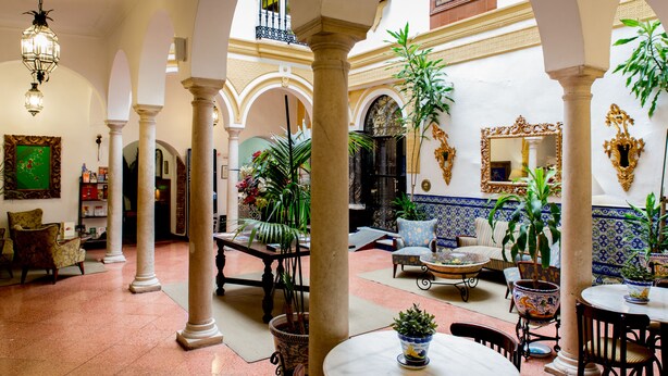 Un patio amplio con columnas, plantas en macetas y un área de comedor con mesas y sillas.