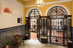 Un vestíbulo de hotel con puertas de hierro negras ornamentadas, suelo de baldosas y un cartel del Hotel Abarico.