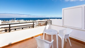 Un balcon avec des chaises blanches et une table, d’où l’on peut admirer le paysage urbain qui s’étend le long de la côte.