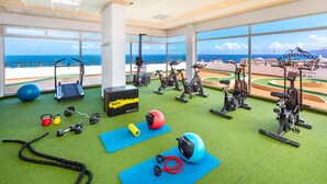 Une salle de sport équipée de matériel d’exercice, avec un tapis bleu et une vue sur l’océan.