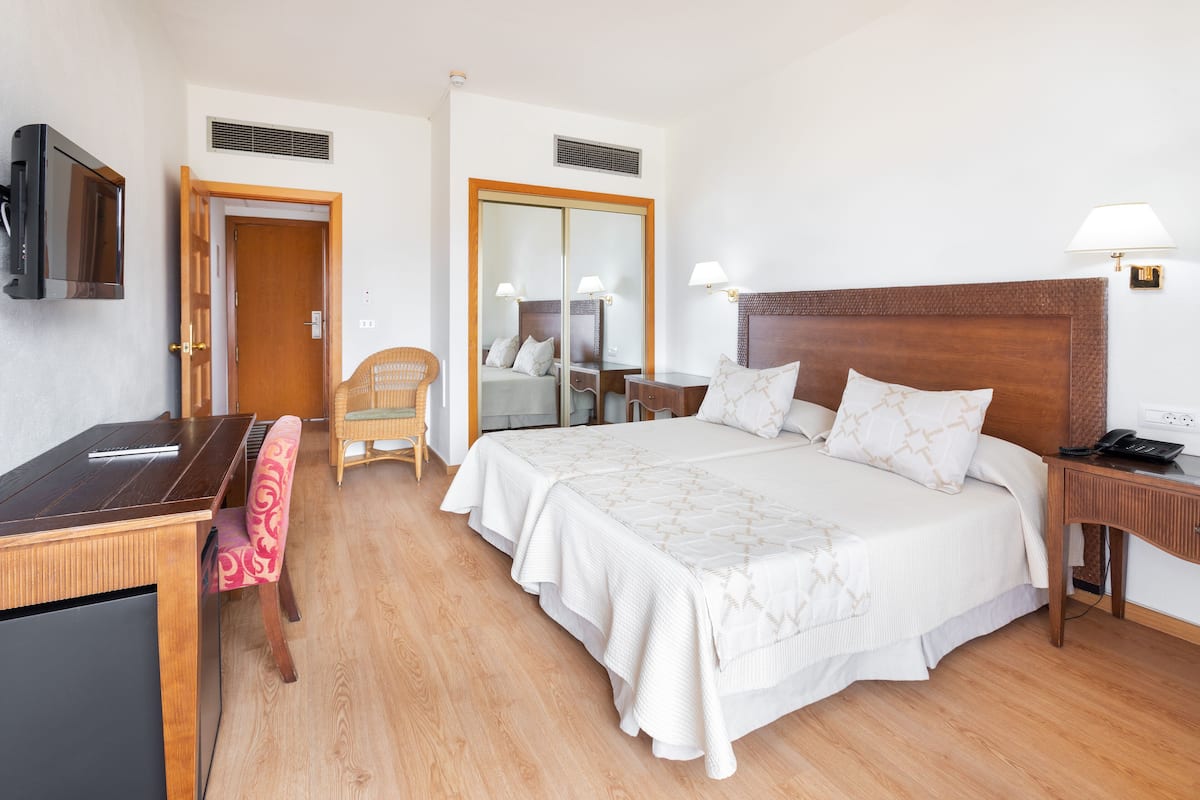 Une chambre d’hôtel comprenant un lit, une table de chevet, une chaise, un bureau, une télévision et une armoire.