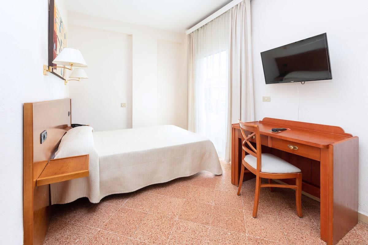 Une chambre d’hôtel comprenant un lit, un bureau avec une chaise, une télévision et une lampe fixée au mur.