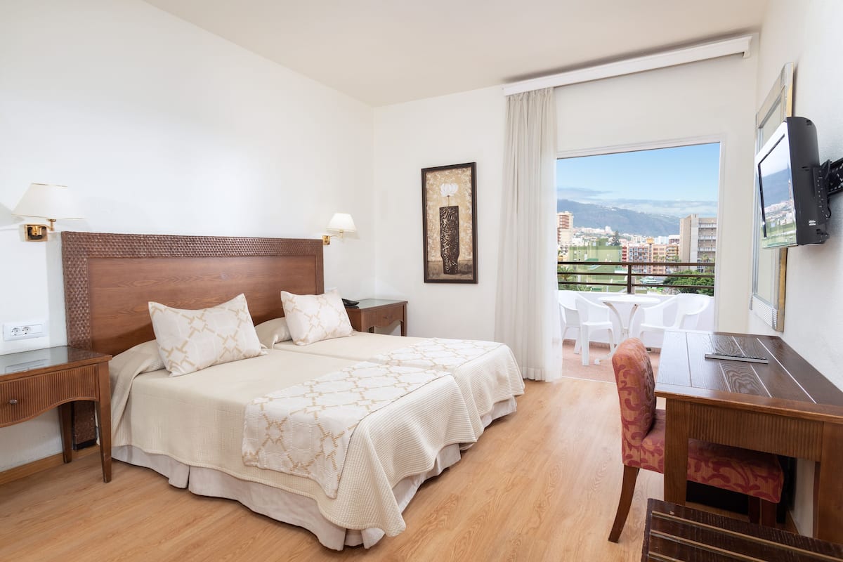 Une chambre d’hôtel avec un grand lit, un bureau, une chaise, une télévision et un balcon offrant une vue sur la ville.