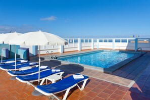 Area piscina con sedie a sdraio e ombrelloni, cielo azzurro e vista sul mare.