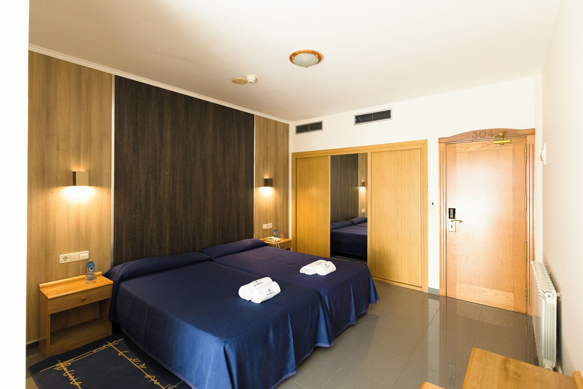 Habitación de hotel con dos camas, paneles de madera, una puerta de madera y un radiador.