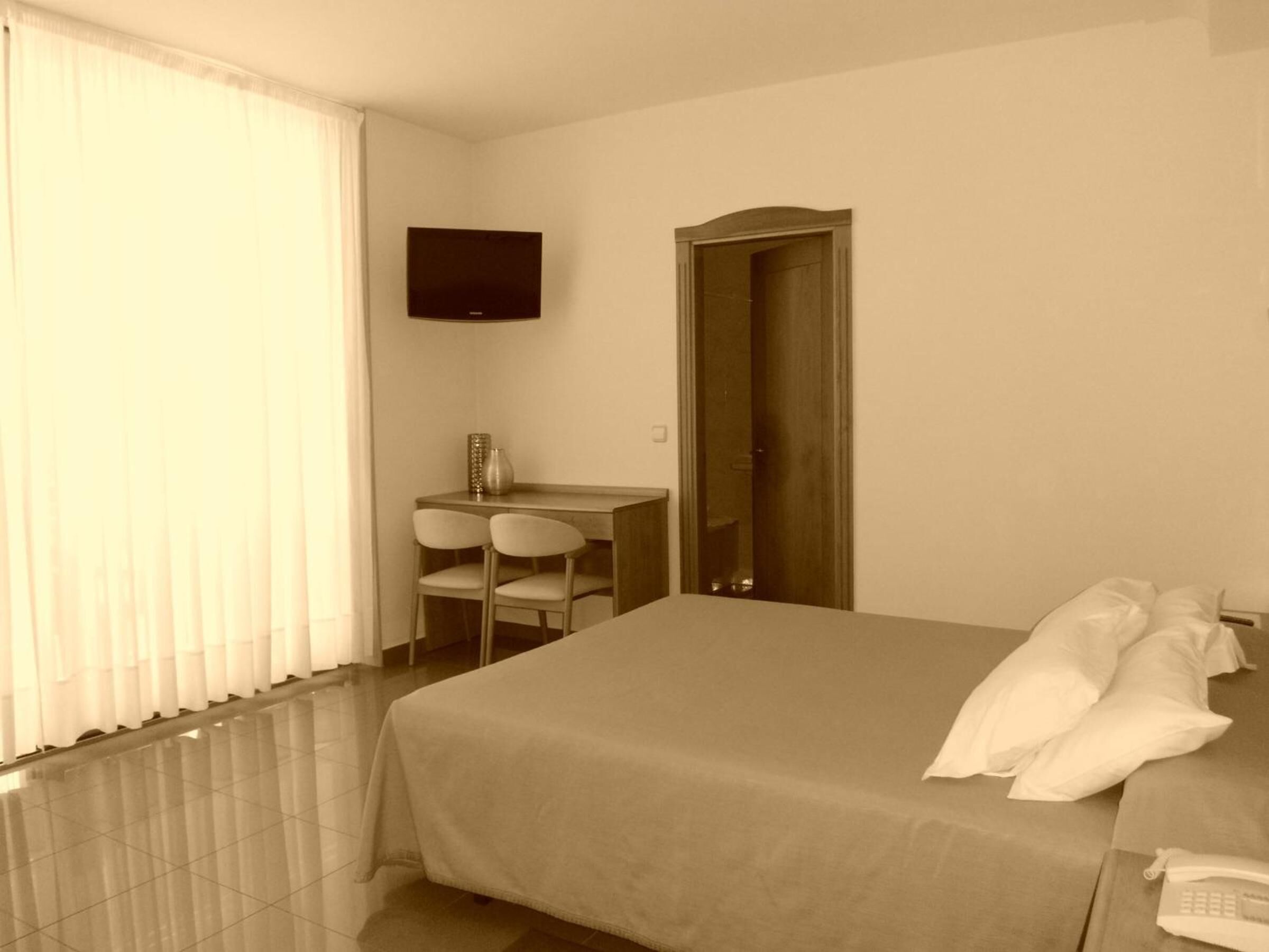 Een hotelkamer met een bed, een bureau met twee stoelen, een televisie aan de muur en een deur.