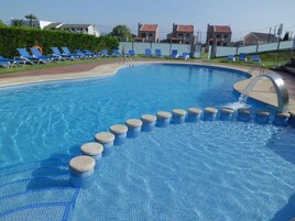 Una piscina al aire libre, sombrillas, sillones reclinables de piscina