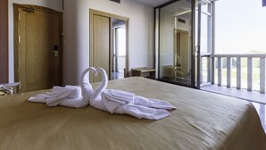Habitación de hotel con cama, puerta de madera, espejo y balcón con vistas.
