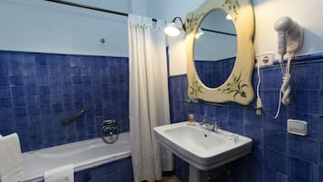 Un baño con bañera, lavamanos, espejo y secador de pelo en la pared.