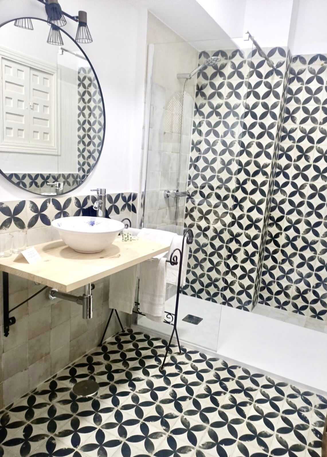 A bathroom with a round mirror, a sink, a shower, and patterned tiles.