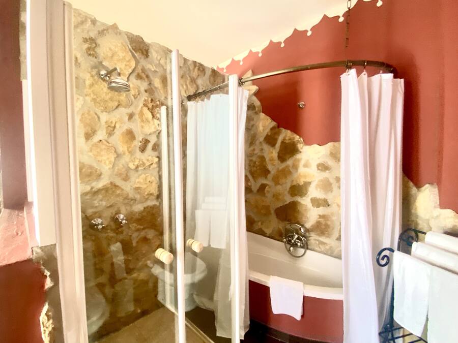 Un baño con pared de piedra, lavamanos blanco y ducha con puerta de vidrio.
