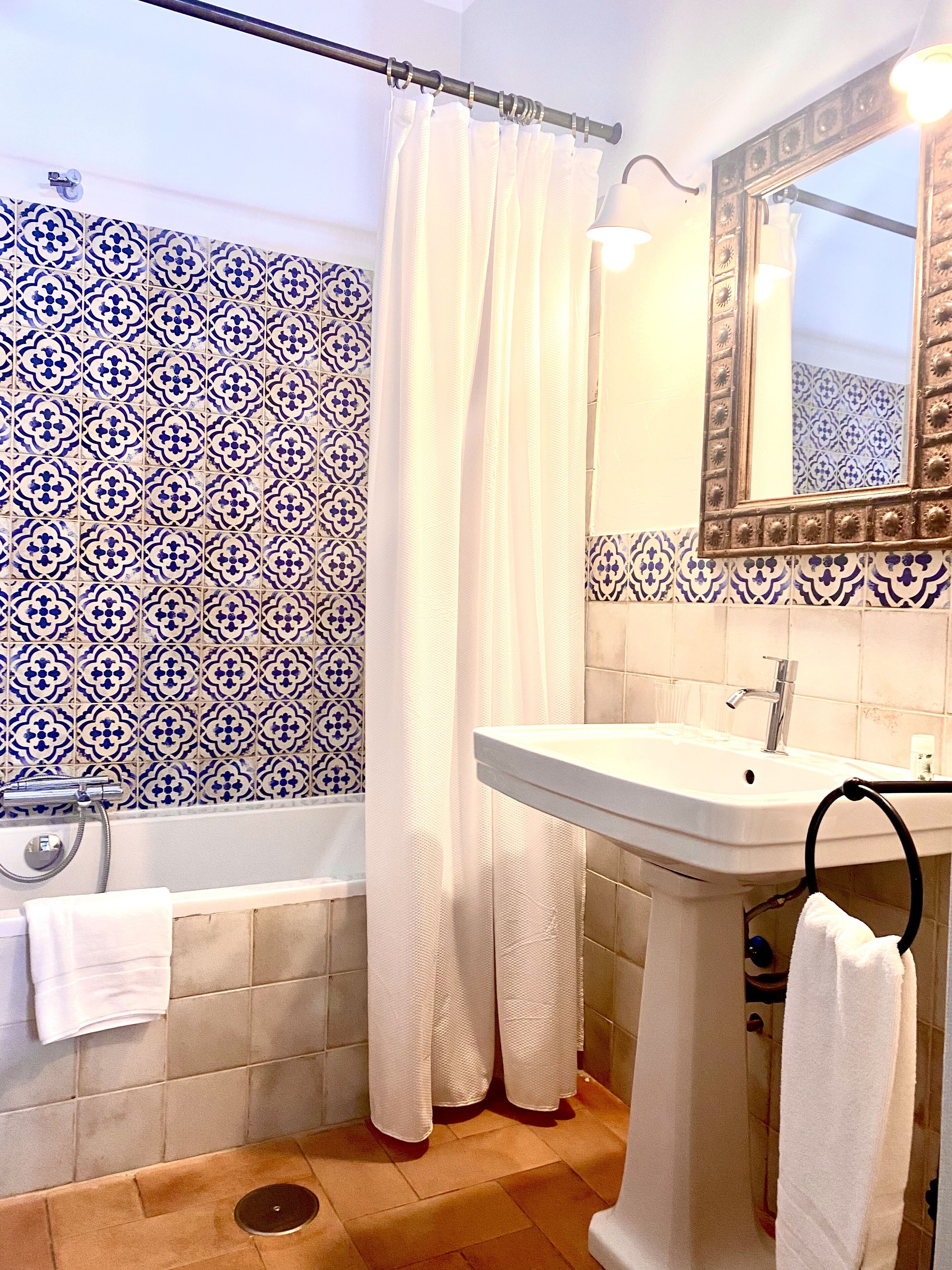 A bathroom with a white bathtub, a white sink, a shower curtain, and a mirror with a decorative frame.