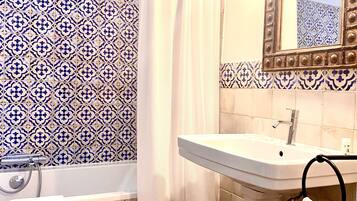 A bathroom with a white bathtub, a white sink, a shower curtain, and a mirror with a decorative frame.