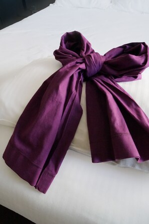 Un lit avec un oreiller blanc et une couverture violette nouée.