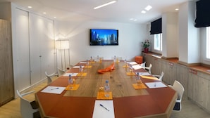 Una sala de conferències amb una taula ovalada gran, caires blancs i una televisi ó penjada a la paret.