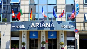 Hotel anomenat "ARIANA" amb diverses banderes, incloent-hi la bandera suïssa, i un senyal que indica un límit de 30 minuts per aparcar.