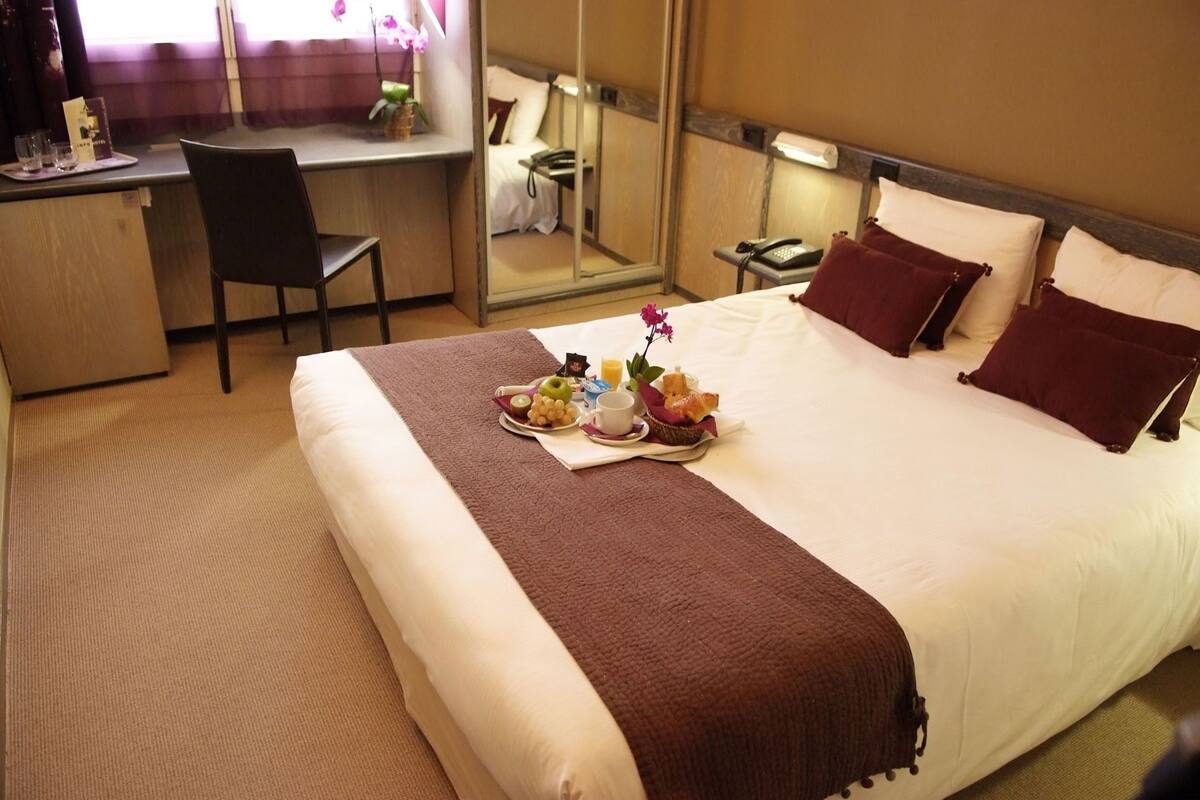 A hotel room with a bed, a desk, a chair, and a small table with a tray of breakfast items.