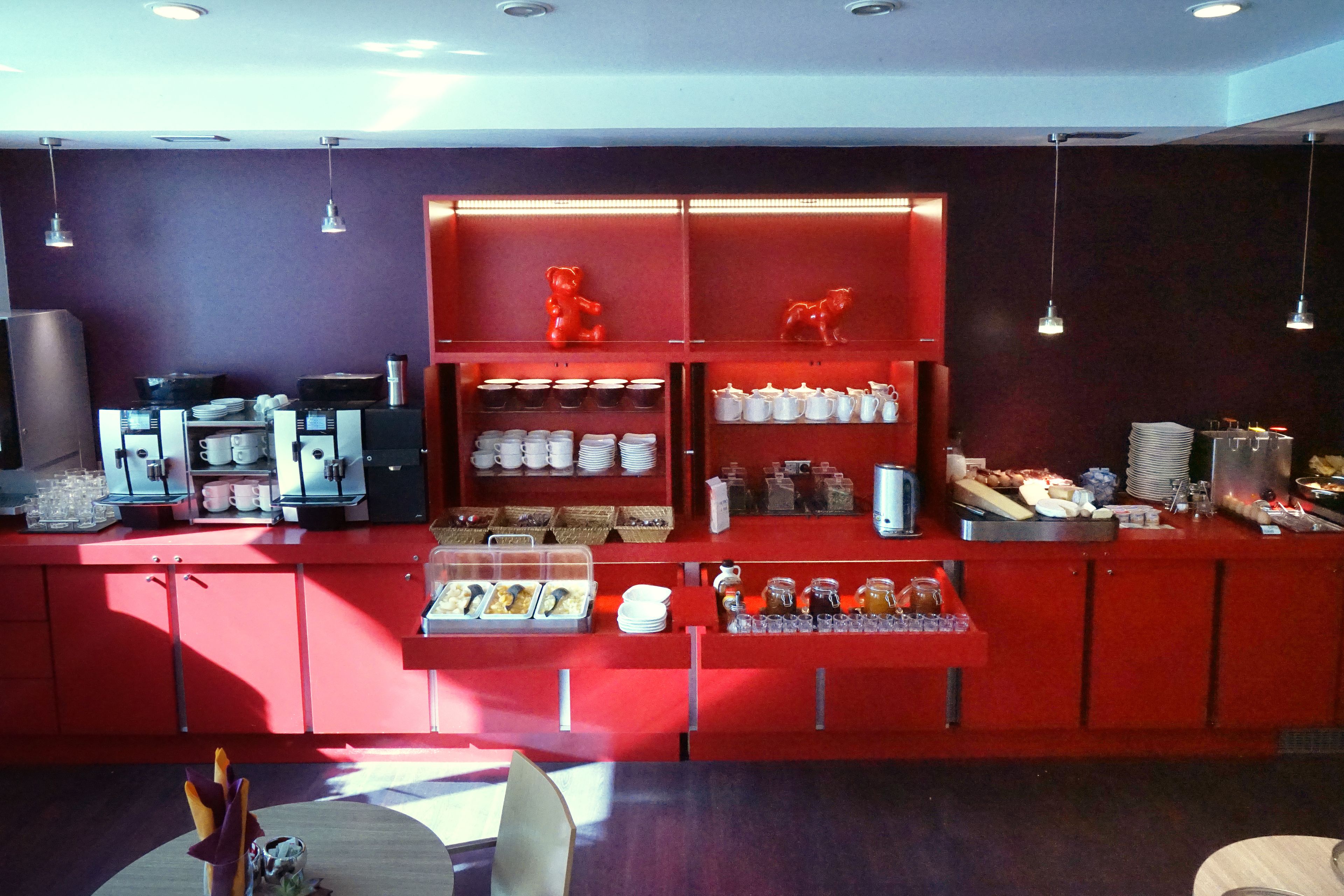 A breakfast bar with a red color scheme, equipped with coffee machines, tea pots, and various breakfast items.