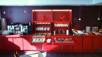 A breakfast bar with a red color scheme, equipped with coffee machines, tea pots, and various breakfast items.