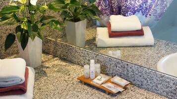 A bathroom with a granite countertop, a white sink, a mirror, a potted plant, towels, and toiletries.