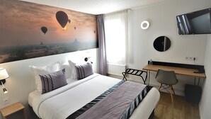 Quarto de hotel com cama, escrivaninha, televisão e pintura de balões de ar quente.
