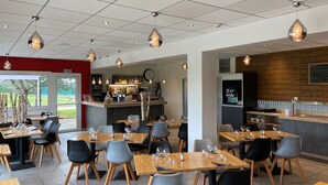 A modern restaurant interior with wooden tables and chairs, a bar area, and a view of the outdoors.