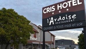 A sign for 'CRIS HOTEL' and 'l'Ardoise RESTAURANT' with a clear view of the building and parked cars.