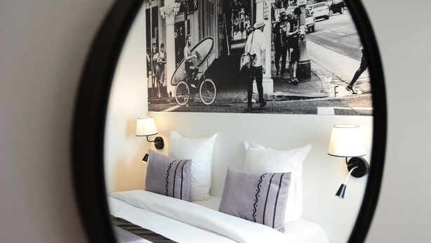 Quarto de hotel com cama, almofadas e uma luminária fixada na parede.