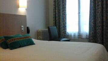 Habitación de hotel con una cama grande, cabecero, luz de pared, radiador, una silla y una ventana con cortinas.