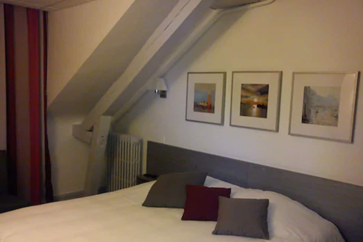 Un dormitorio con una cama, un radiador y tres cuadros en la pared.
