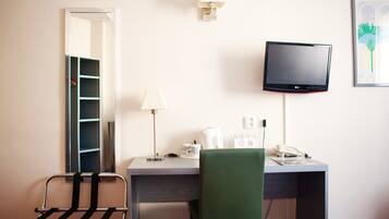 A hotel room with a desk, chair, lamp, phone, and a TV mounted on the wall.