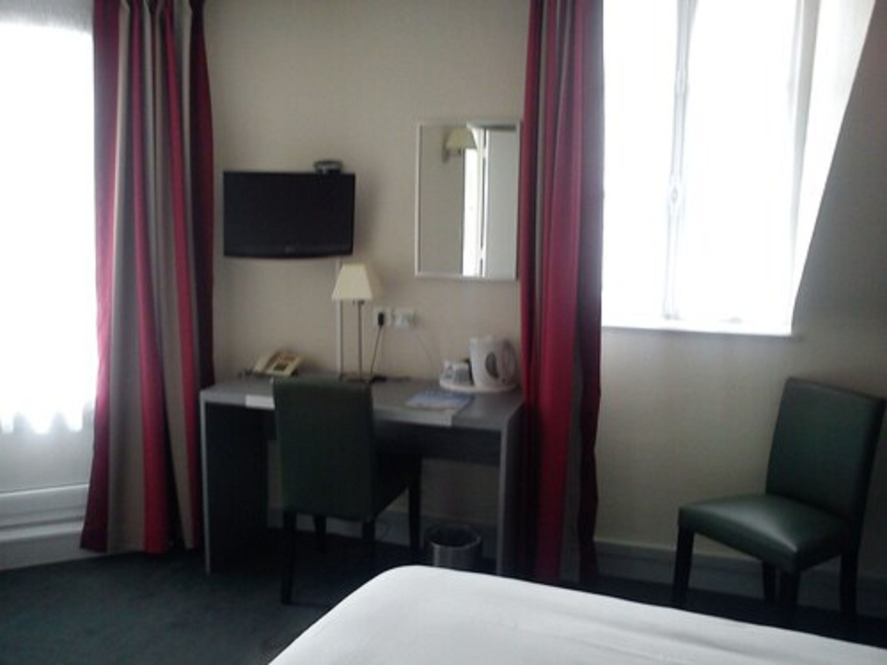Una camera d'albergo con un letto, una scrivania con una sedia, una televisione, una lampada e una finestra con tende.