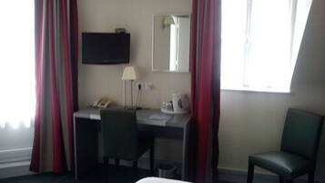 Una camera d'albergo con un letto, una scrivania con una sedia, una televisione, una lampada e una finestra con tende.