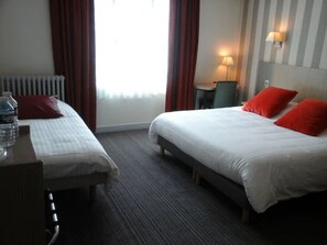 A hotel room with two beds, a desk, a chair, a lamp, and a radiator. - Hotel Carmin (Le Havre)