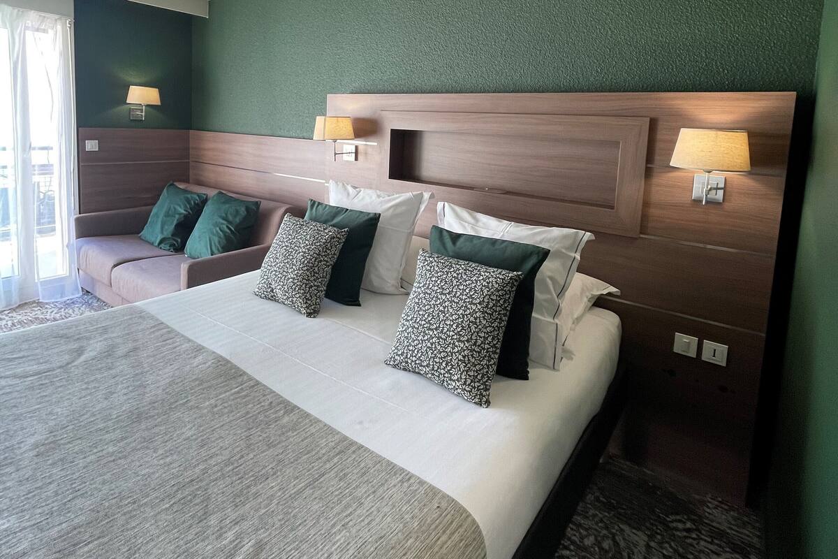 A hotel room with a large bed, two bedside tables with lamps, a green accent wall, and a view of the outdoors.
