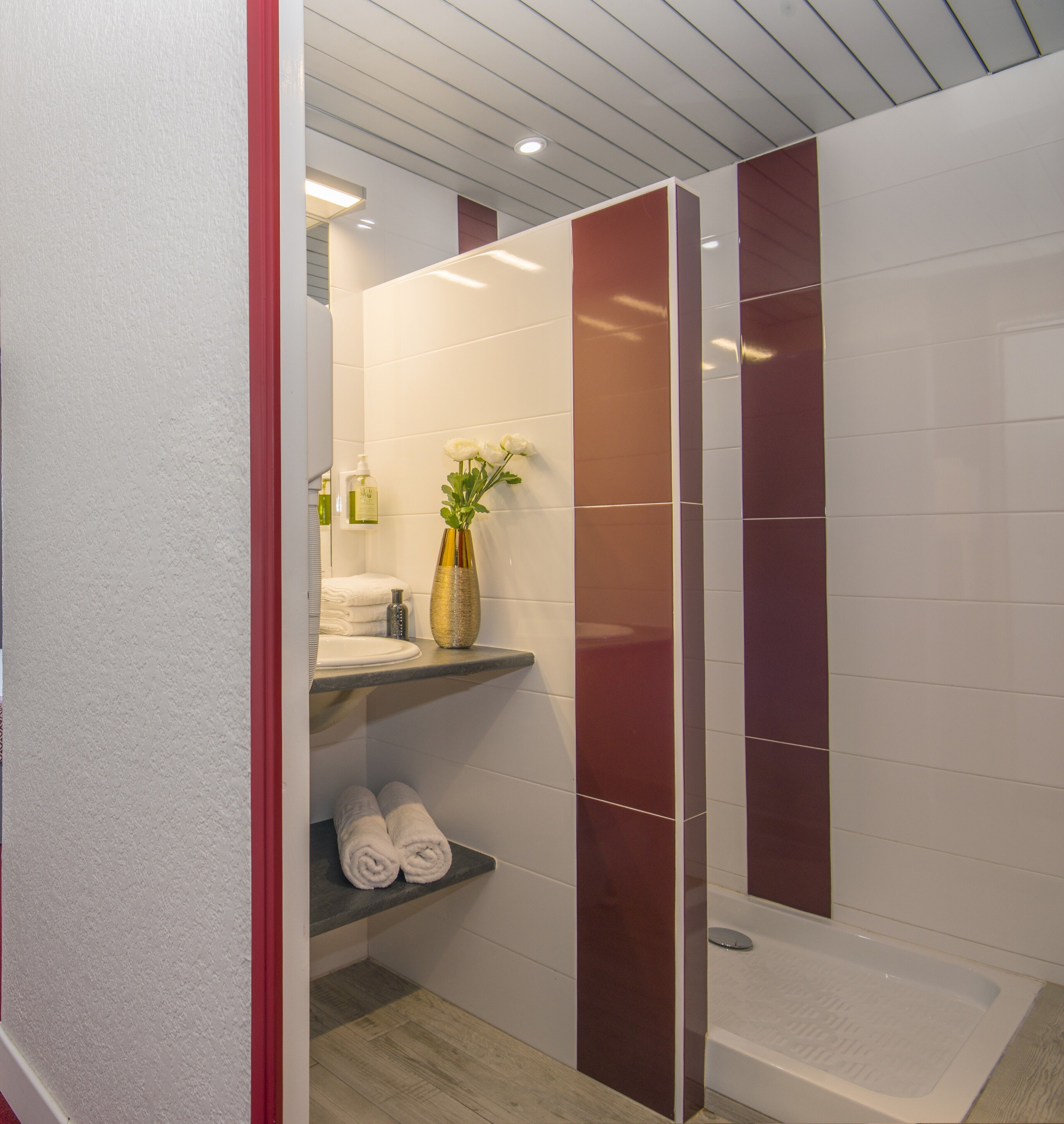 Un baño moderno con cabina de ducha de vidrio, tocador con espejo y repisa con toallas y artículos de aseo.