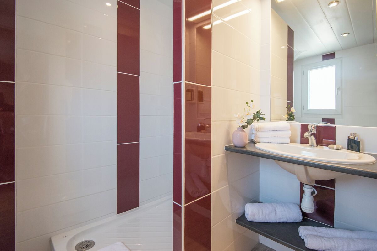 Un baño moderno con lavamanos blanco, azulejos de mármol y cabina de ducha de vidrio.