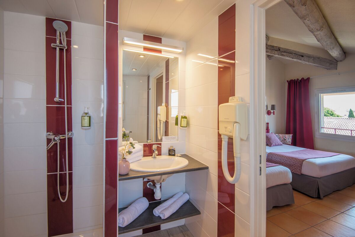 Un bagno con doccia, lavabo e specchio. Nella stanza adiacente, un letto con finestra e tende.