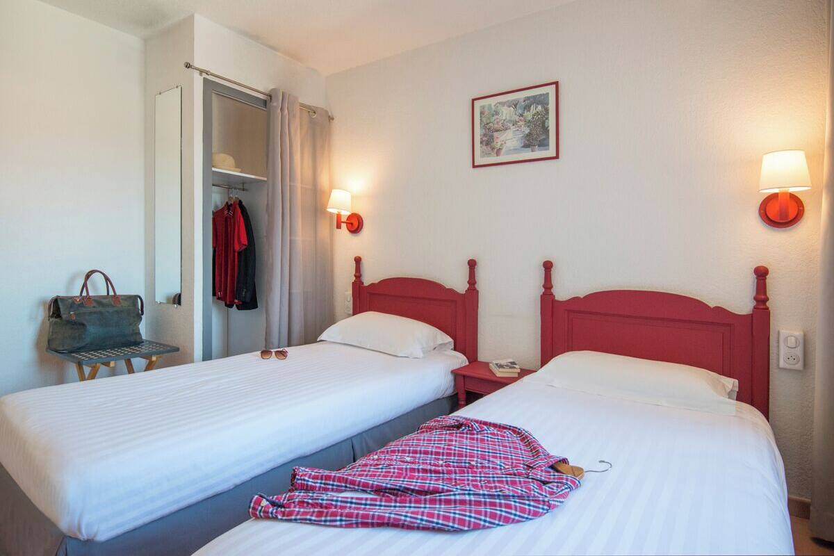 A hotel room with two single beds, a wardrobe, a chair, and a lamp.