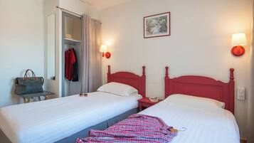 A hotel room with two single beds, a wardrobe, a chair, and a lamp.