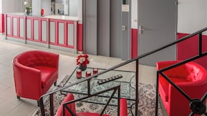 Eine moderne Lobby mit roten Sitzgelegenheiten, einem Empfangstresen und einer Treppe.