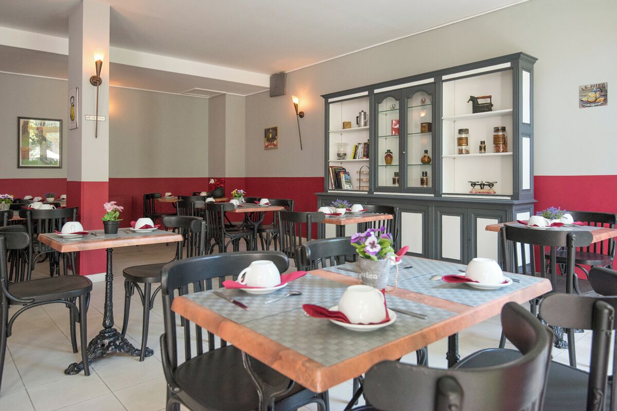 Un restaurante con varias mesas y sillas, un aparador grande con puertas de cristal, y una decoración roja y blanca en las paredes.