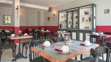 Un restaurante con varias mesas y sillas, un aparador grande con puertas de cristal, y una decoración roja y blanca en las paredes.
