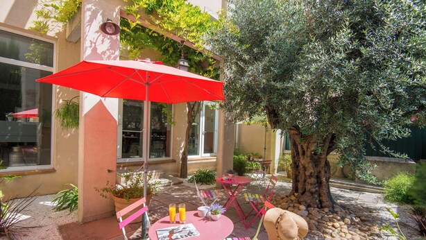 Eine Terrasse im Freien mit einem roten Sonnenschirm, einem runden Tisch und Stühlen sowie einem großen Baum.