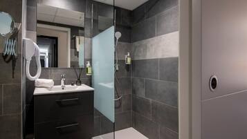 A modern bathroom with a glass shower enclosure, a vanity with a mirror, and dark tiled walls.