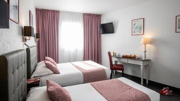 Une chambre d’hôtel avec deux lits, un bureau, une chaise, une télévision et une fenêtre avec des rideaux.