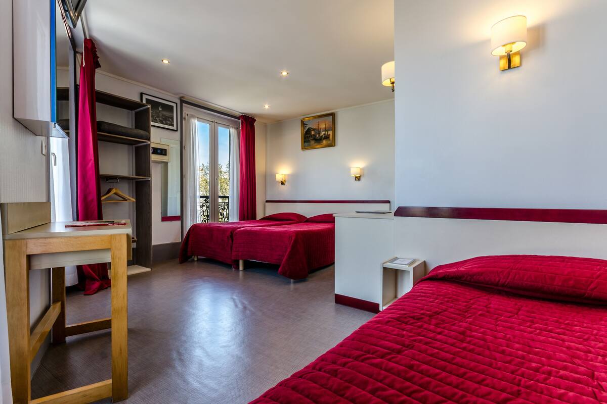 A hotel room with two beds, a wooden desk, and a wardrobe.