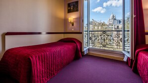 Una habitación de hotel con dos camas, un ventanal con vistas a un edificio histórico y una lámpara de pared decorativa.