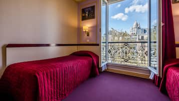 A hotel room with two beds, a large window with a view of a historic building, and a decorative wall lamp.